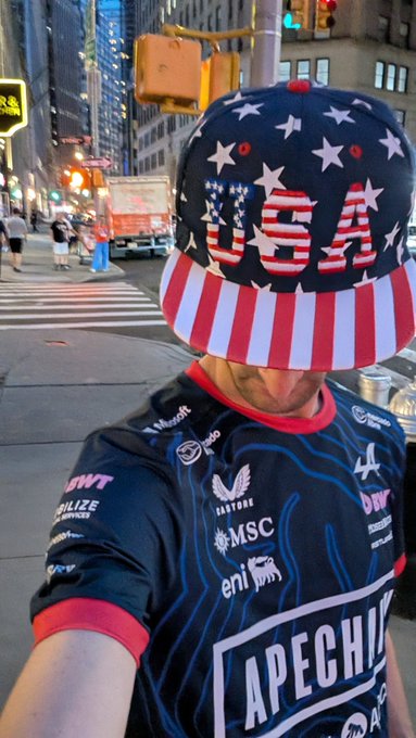 A person wearing a USA-themed stars-and-stripes baseball cap and a Napoli soccer jersey (featuring "APECHIN" sponsor text and logos like Castore, MSC, and eni) poses for a selfie on a New York City street, visually blending American patriotism with their representative style as mentioned in the bio.