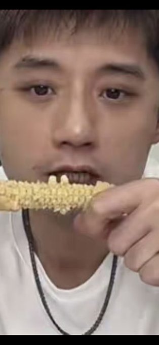 A close-up of a young man taking a bite out of a stick covered in puffed grains or rice cereal.
