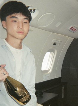 A young man in a white hoodie poses inside what appears to be a private jet, with a visible "EXIT" sign and aircraft window in the background. The image relates to the post about a crypto influencer nicknamed "Kimchi," who posted on July 22 and preceded a 22.8% Bitcoin price increase to $81,100 over the following 60 days.