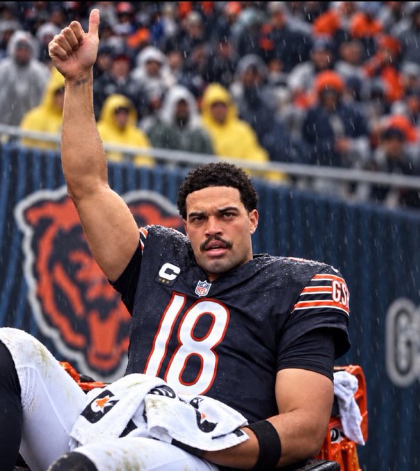 Chicago Bears player #18 gives a thumbs up while sitting on the bench in the rain during a game.
