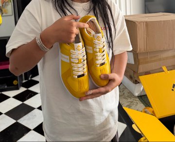 A person holds up a pair of yellow high-top sneakers with white laces, gifted by Binance. The caption "Thanks for the shoes from Binance! Shoes gifted by @binancezh!" matches the image, showing a fan or recipient proudly displaying branded footwear received from the cryptocurrency exchange.