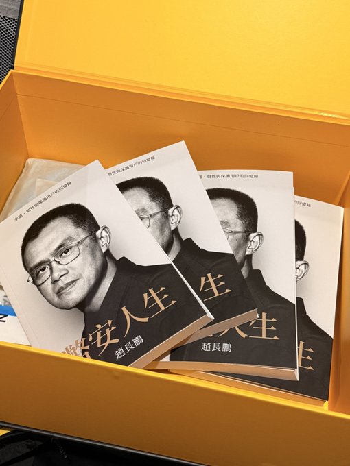 The image features an open yellow box containing three books with Chinese writing on them. The books are titled "Binance Life" and appear to be memoirs written by Binance founder CZ, who wrote about his experiences while serving time in a U.S. prison. The books are arranged neatly inside the box, showcasing their covers and titles for easy identification.