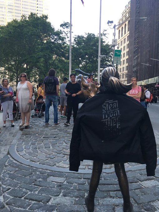 A person wearing a black 'Steal from the rich' jacket with a llama costume walks through a busy city plaza (Flatiron area) with pedestrians nearby.