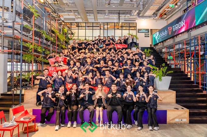 A large group photo of people posing together at a Bitkub Academy event, with signage for Bitkub and Tron visible in the background.