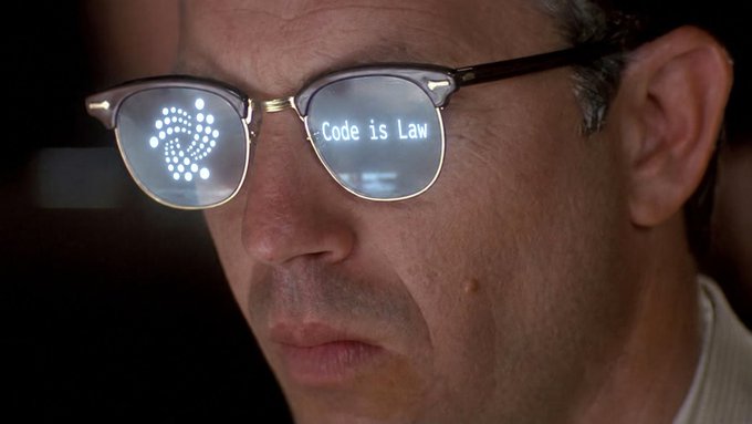 A close-up of a man's face wearing glasses that display a fingerprint graphic and the text 'Code is Law' reflected in the lenses.
