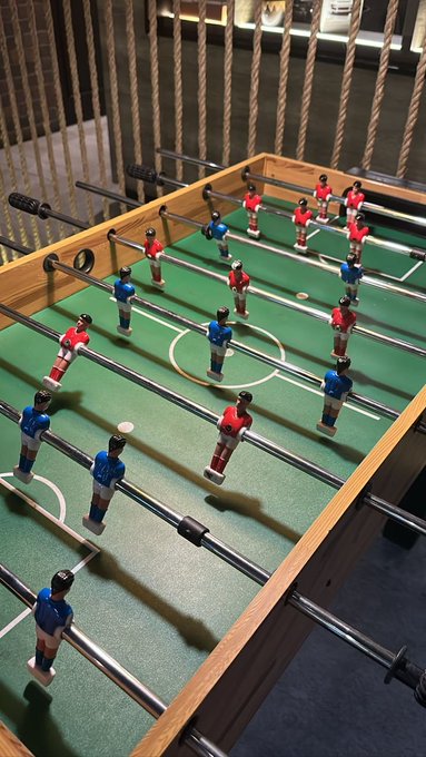 A foosball table with player figurines in red and blue uniforms set up for a game on a green playing surface.