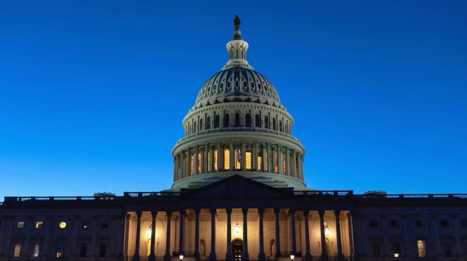 The image shows the U.S. Capitol building illuminated against a deep blue evening sky, with its iconic dome and columns prominently featured. The post about congressional activity ties directly to this setting, as it references upcoming legislative events including Federal Reserve Chair Kevin Warsh's crypto-related congressional testimony scheduled for the 15th.