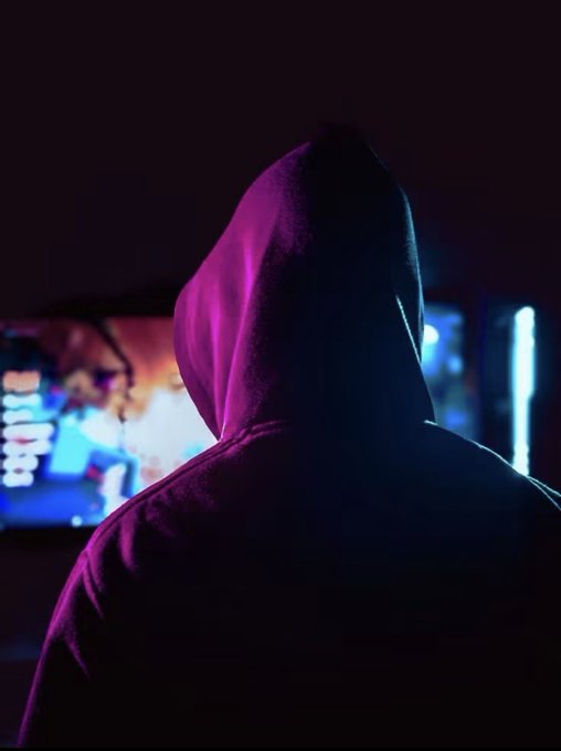 A silhouetted figure in a hooded sweatshirt faces a glowing monitor displaying blurred content, illuminated by magenta and teal neon lighting in a dark room. The mysterious, anonymous posture visually reinforces the post's discussion of meeting "KYC & Community Momentum" thresholds and the secretive, underground nature of crypto projects.