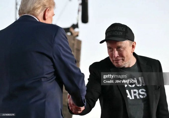 A man wearing a "Make America Great Again" cap shakes hands with Donald Trump, whose face is partially visible from behind. The man's t-shirt reads "OCCUPIED MARS," and the image appears to be used to accompany a caption questioning his projects and business ventures.

Credit: JIM WATSON/AFP via Getty Images.