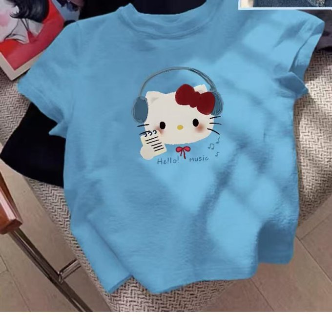A light blue t-shirt featuring Hello Kitty wearing headphones and holding a microphone with the text "Hello! music" is displayed on a textured surface. While the post mentions "保持内裤干燥" (Keep underwear dry), the image shows a shirt seemingly meant to help keep the wearer dry beneath the "Hello! music" graphic.