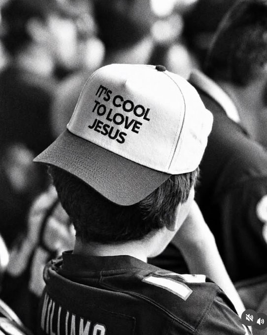 A black-and-white photo from behind of a child wearing a white cap with the text 'IT'S COOL TO LOVE JESUS'.