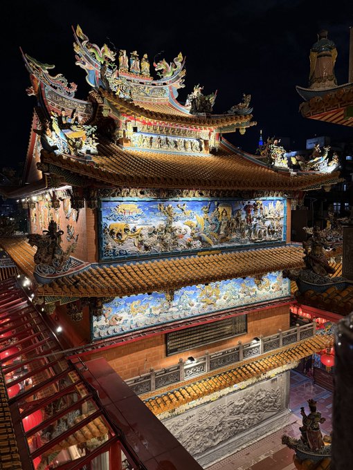 An ornate, multi-tiered Chinese temple or shrine glows vibrantly at night, featuring intricate dragon sculptures, colorful ceramic roof tiles, and elaborate relief murals depicting mythological scenes, with red lanterns lining a staircase on the left. The post's sleepy "Gn 😴" caption suggests a peaceful nighttime moment appreciating the temple's illuminated beauty as a serene way to end the day.