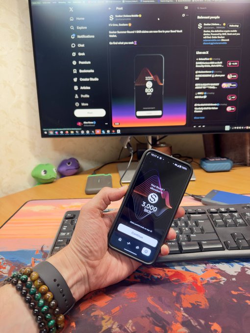 A person holding a smartphone showing a '3,000 SKR' claim screen for the Seeker S1 device, with a computer monitor in the background displaying the Seeker X (Twitter) post about extending summer round 1 SKR claims.