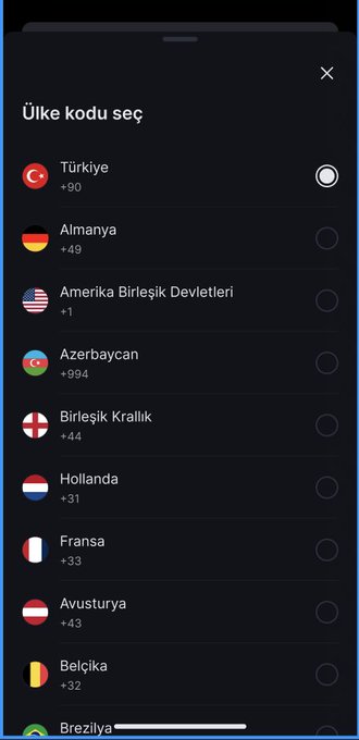 A mobile phone screen displays a "Ülke kodu seç" (Select country code) menu with a list of countries in Turkish, including Türkiye (+90), Almanya (+49), Amerika Birleşik Devletleri (+1), Azerbaycan (+994), Birleşik Krallık (+44), Hollanda (+31), Fransa (+33), Avusturya (+43), and Belçika (+32), with Türkiye currently selected. The image relates to the post by illustrating an investment platform's user registration interface, emphasizing how accessibility through simple country selection makes financial tools available to users across multiple regions worldwide.