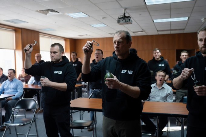 A group of men wearing "BIP-110" hoodies practice drawing and deploying what appear to be improvised explosives from tin cans in a classroom setting. The image satirically portrays BIP-110 participants engaged in unconventional training exercises.