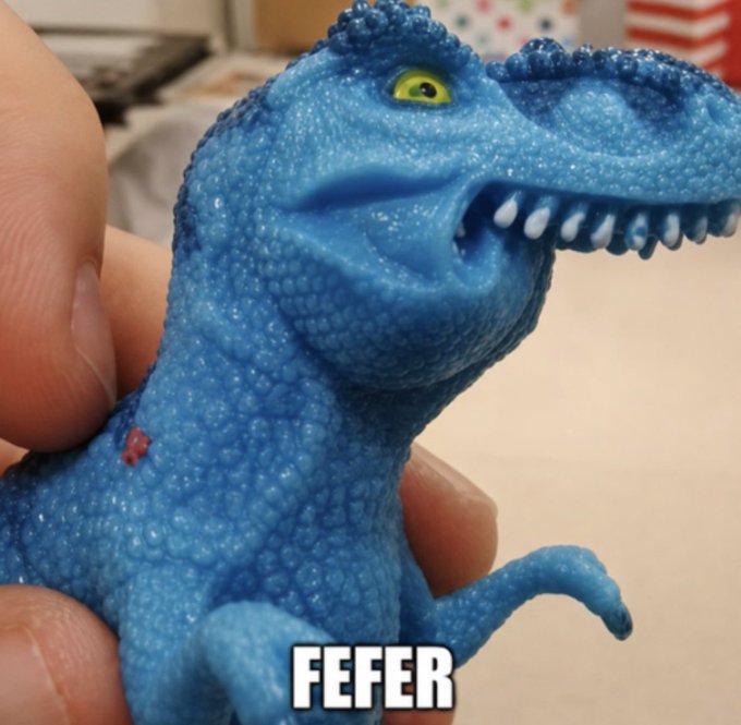 A hand holding a small blue toy dinosaur with the text 'FEFER' at the bottom.
