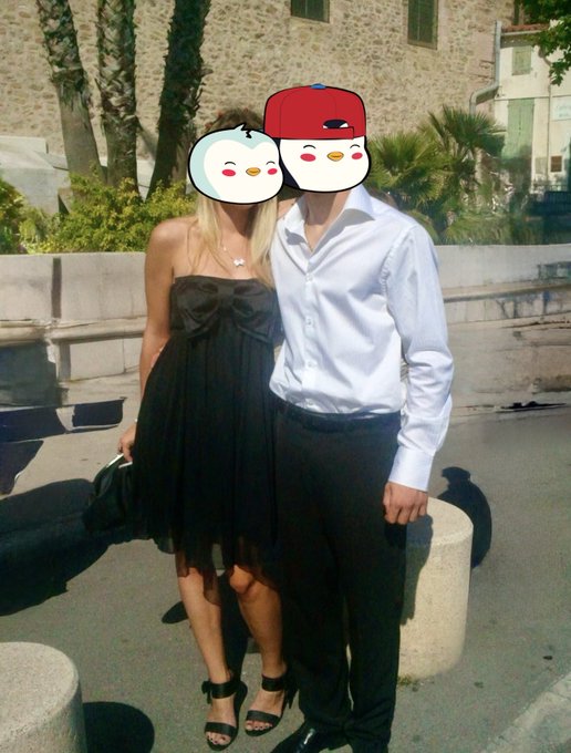 A couple poses together outdoors, with their faces obscured by cartoon emoji stickers—a white bird and a red baseball cap.