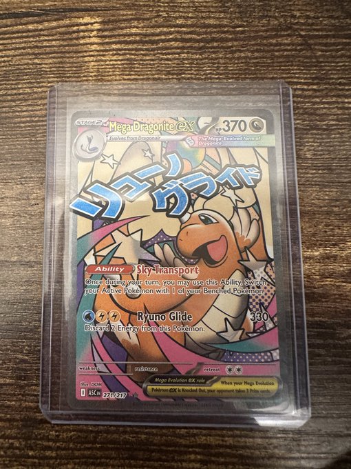 A Japanese Pokemon trading card featuring 'Mega Dragonite ex' (HP 370) with the abilities 'Sky-Transport' and 'Ryuno Glide' (380 damage), displayed in a protective sleeve on a wooden surface.