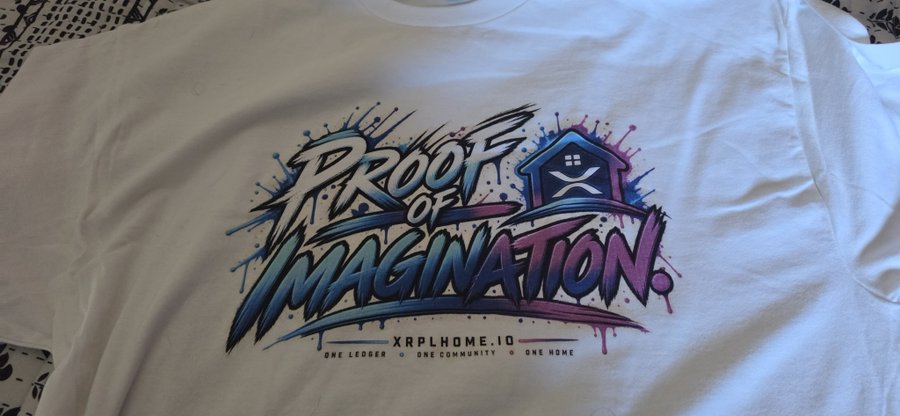 A white t-shirt featuring the colorful graffiti-style 'Proof of Imagination' logo for XRPLHOME.IO, with the tagline 'ONE LEDGER • ONE COMMUNITY • ONE HOME'.