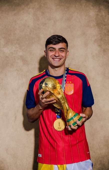 A young man in a red and yellow striped soccer jersey smiling while holding the FIFA World Cup trophy along with a winner's medal.