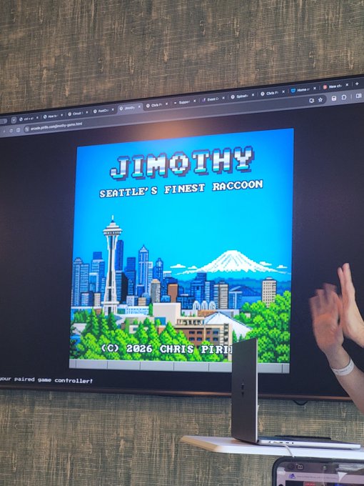 A large display screen shows the pixel-art title screen for "JIMOTHY - SEATTLE'S FINEST RACCOON" featuring the Seattle skyline with the Space Needle and Mount Rainier, credited to Chris Pirit (2026). The image ties to the post "Oh, btw, Jimothy is still big" by showcasing its eye-catching title screen being showcased on a big screen, with hands gesturing toward it.
