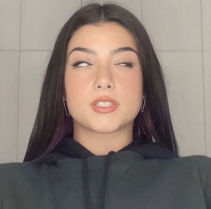 A close-up portrait shows a woman with long dark hair, makeup, and hoop earrings looking sideways against a pale tiled background.