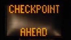 An electronic road sign displays 'CHECKPOINT AHEAD' in bright orange LED letters against a dark background.
