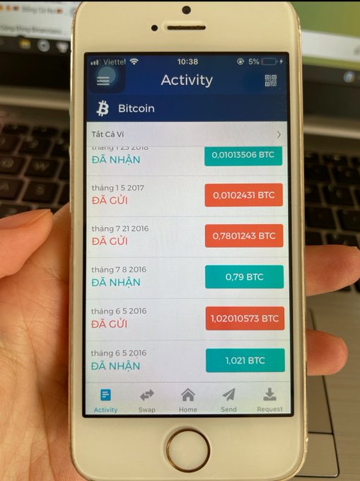A hand holds an iPhone displaying a Bitcoin wallet app activity log in Vietnamese, showing received (ĐÃ NHẬN) and sent (ĐÃ GỬI) transactions in BTC.