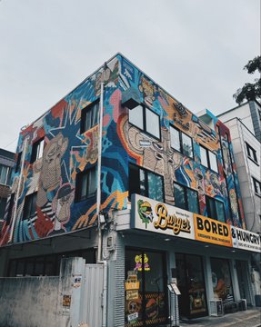 A vibrant street art mural covers the corner of a building housing "Loveya's Bored & Hungry" vegan restaurant, featuring colorful abstract figures.