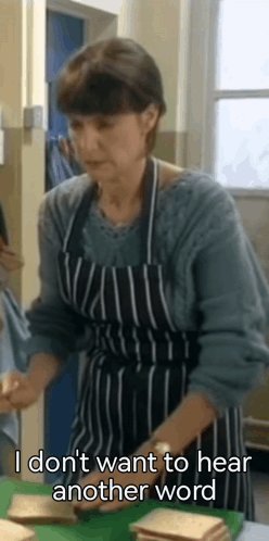 The image shows an older woman wearing an apron, standing at a table with two sandwiches placed on it. The text "I don't want to hear another word" is written above her head, indicating that she does not want to hear any more words or engage in further conversation.