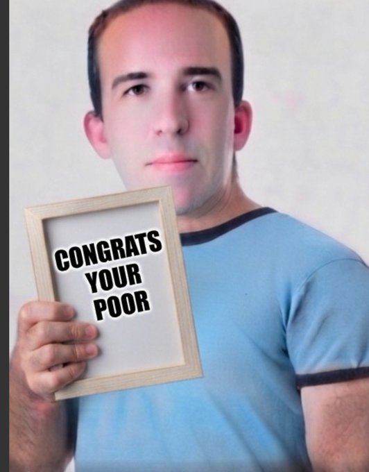 A man with short hair wearing a blue t-shirt holds up a framed sign that reads 'CONGRATS YOUR POOR'.