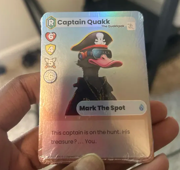 A hand holds a holographic trading card featuring 'Captain Quakk, The Quackspear' with stats for 'Mark The Spot'.