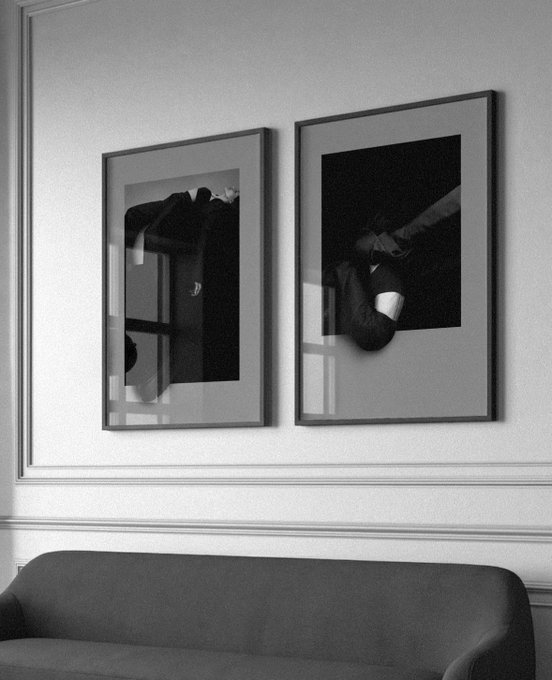 A black and white photograph showing two framed black and white pictures hanging on a wall above a dark sofa, with reflections visible on the glass.