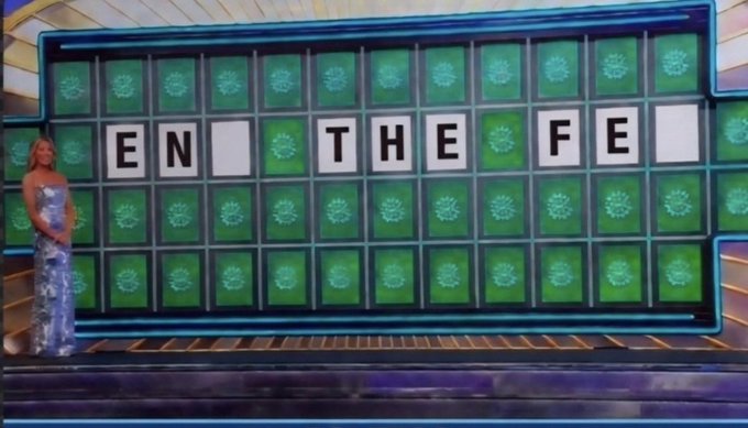 A blonde woman in a sparkly silver dress stands next to a "Wheel of Fortune" game board displaying the revealed letters "EN_THE_FE_". The image connects to the "GM" (Good Morning) greeting by inviting viewers to solve the puzzle, likely spelling out "ON THE FENCE" or a similar phrase.