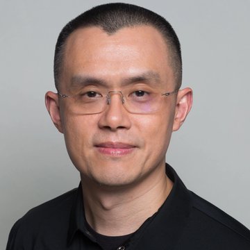 A portrait photograph of a man with short hair wearing glasses and a black polo shirt against a gray background.