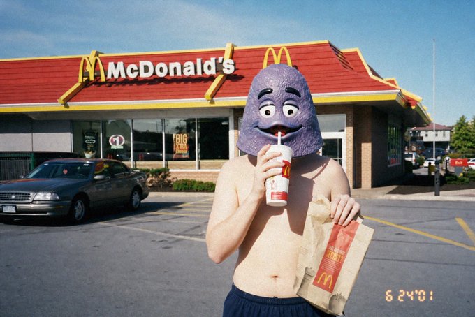 A shirtless man wearing a purple Grimace mascot mask stands in front of a McDonald's restaurant, drinking from a cup and holding a paper bag with the golden arches logo, dated 6/24/01. The image's relevance to the "gm" post appears to be an inside joke or meme reference, possibly relating to the man's unusual acquisition of the Grimace costume or a play on McDonald's branding.