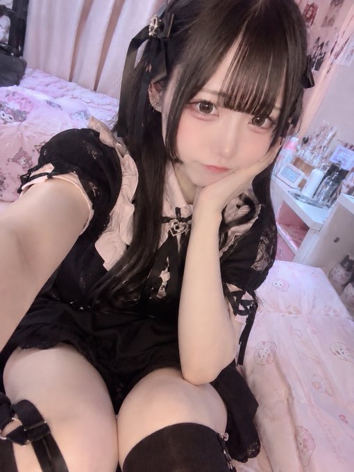 A selfie of a person in an elaborate gothic-lolita black dress with lace and ruffled details, sitting in a pink bedroom and resting their chin on their hand.