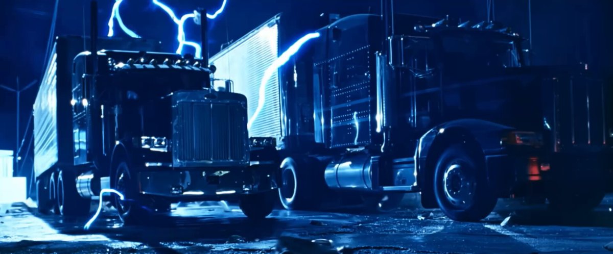 The image shows two semi-trucks parked next to each other at night, with one truck being black and the other being silver. The trucks are positioned side by side, facing opposite directions. In front of the silver truck, there is a person standing on the sidewalk. The background features a dark sky filled with lightning bolts, creating an intense atmosphere in the scene.