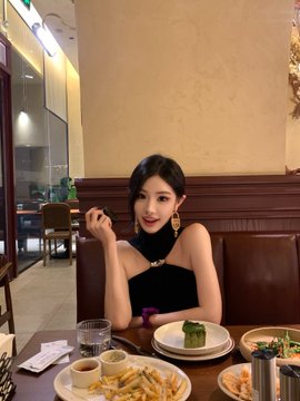A stylish woman in a black halter top poses at a restaurant table filled with plates of food and fries. The caption's playful invitation to "bump into me in 2049" pairs with the image's cozy dining setting, suggesting a casual yet charming moment worth meeting up over a meal.