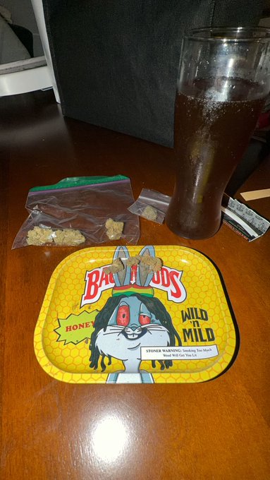 A Bunny Moods 'Wild Mild' Honey flavor CBD edible tray (5mg each, Blood Wild Gsc Sativa) on a wooden table next to a plastic bag with edibles, a lighter, and a glass of soda.