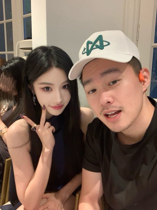 A selfie of a young woman with long dark hair making a peace sign alongside a man wearing a white baseball cap featuring a green "AV" logo, appearing to capture a casual meet-up that aligns with the post about bumping into @0xajc.