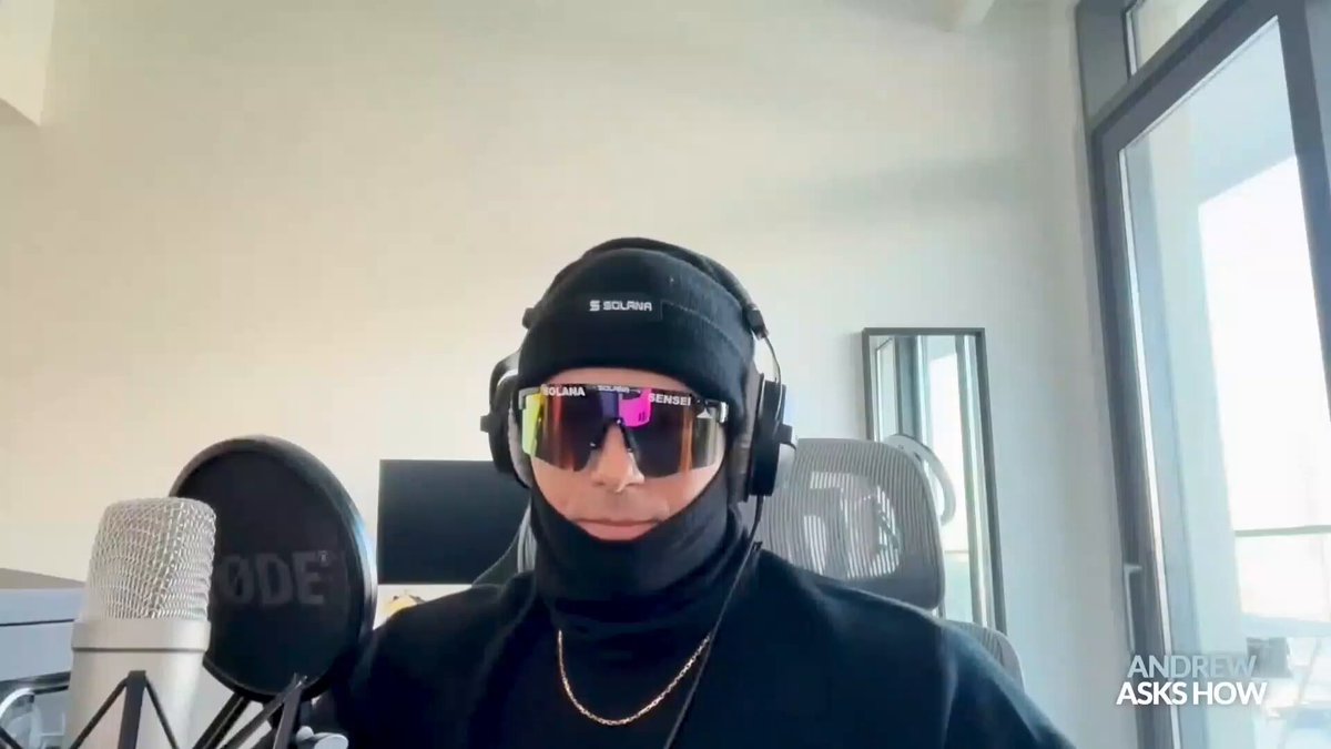 The image features a man wearing sunglasses, a beanie hat, and a necklace, sitting behind a microphone. He appears to be participating in an online gaming event or streaming session. The caption of the image reads "Solana Sensei said rugger with no remorse are getting rewarded while kindhearted builder with unexpected failed project get punished by their own community". This message seems to be related to the game they are playing, possibly a cooperative or competitive one that involves building and managing virtual properties.