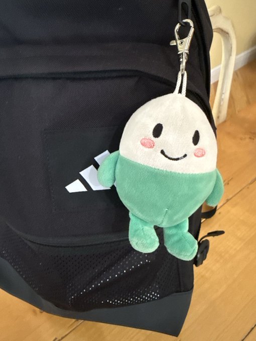 A cute plush toy character hangs from the zipper of a black Adidas backpack, embodying the $cupsey web2 business opportunity.