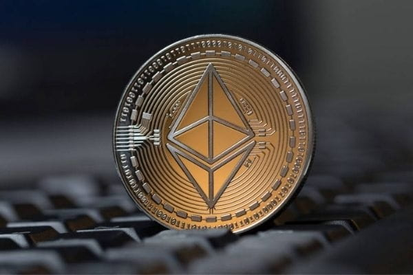 A gold and silver Ethereum coin stands upright on a black keyboard, symbolizing the cryptocurrency's diminishing DEX trading activity. The coin's prominent "ETH" logo connects to the post's discussion of $ETH's spot volume dropping to $29 billion in July, a steep decline from its August 2025 peak.