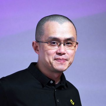 A photo of Binance founder Changpeng Zhao (CZ), wearing glasses and a dark shirt, speaking at what appears to be a formal event with a purple backdrop, accompanying his statement attributing the current crypto downturn to AI investment shifts, geopolitical tensions, and the traditional four-year market cycle.