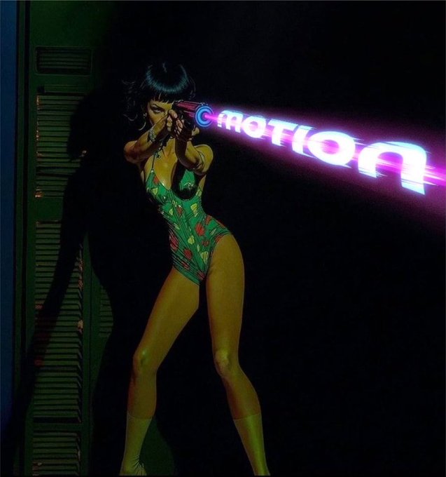 A stylized, poster-like image of a woman in a green floral swimsuit aiming a futuristic gun that fires a glowing pink and blue beam with the word 'EMOTION' written inside it, set against a dark background with green shutters on the left.