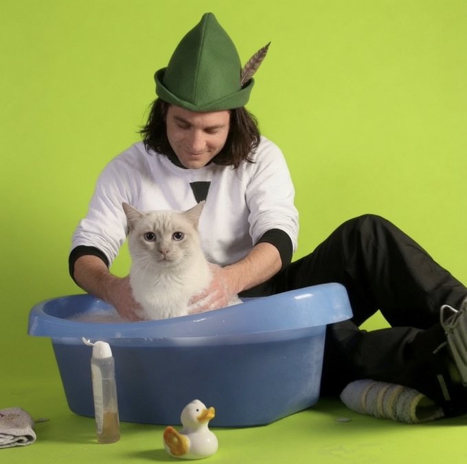 A young man wearing a green Robin Hood-style hat sits on a bright green floor, bathing a white cat in a blue basin alongside a rubber duck and towel. The whimsical scene playfully echoes the "Like Father, Like Son" caption by humorously suggesting the cat is being groomed as Robin Hood's furry sidekick, in a quirky take on the Robinhood Chain metaphor.