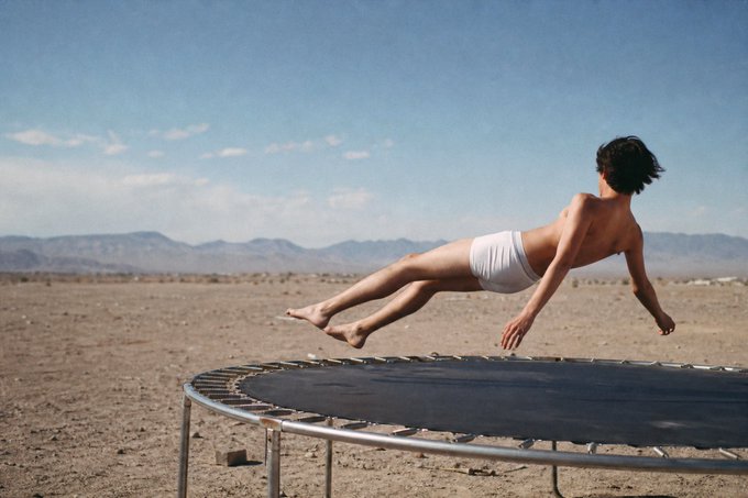 A childhood photo showing a young boy mid-jump on a trampoline in a desert landscape.