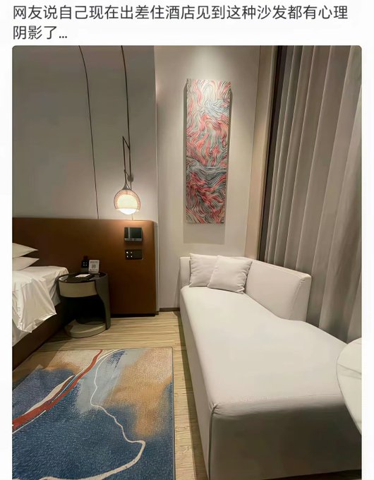 A modern hotel room features a white chaise lounge sofa positioned next to a bed and a colorful abstract artwork, with a decorative rug on the floor. The caption humorously suggests a reluctance to sit on such sofas, alluding to an unspoken rule or concern about their hygiene in hotel settings.