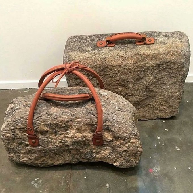 Two handbags designed to look like rough, natural stones are displayed on the floor, with brown leather straps and handles attached to the rocky surfaces.